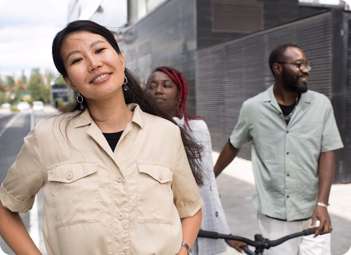 Three people smiling and walking on an urban street; a woman in a beige shirt is in the foreground, while two others are behind her.