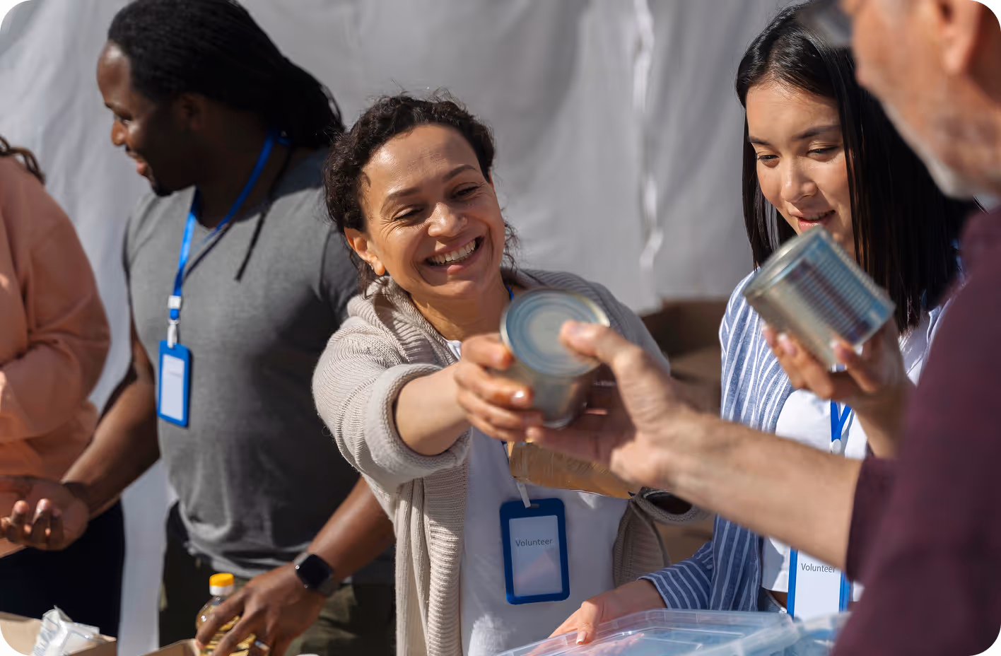 A smiling woman hands over a canned good to someone while other volunteers around her help during a community food donation event.