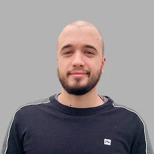 Miembro del equipo de Neocoast con camiseta oscura y barba prolija, mirada serena frente a fondo gris neutro.