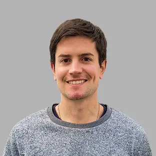 Miembro del equipo de Neocoast con camiseta gris clara, sonrisa amigable y mirada directa, sobre fondo gris neutro.