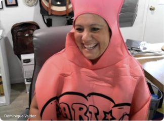 Smiling woman wearing a bright pink costume with decorative lettering indoors.