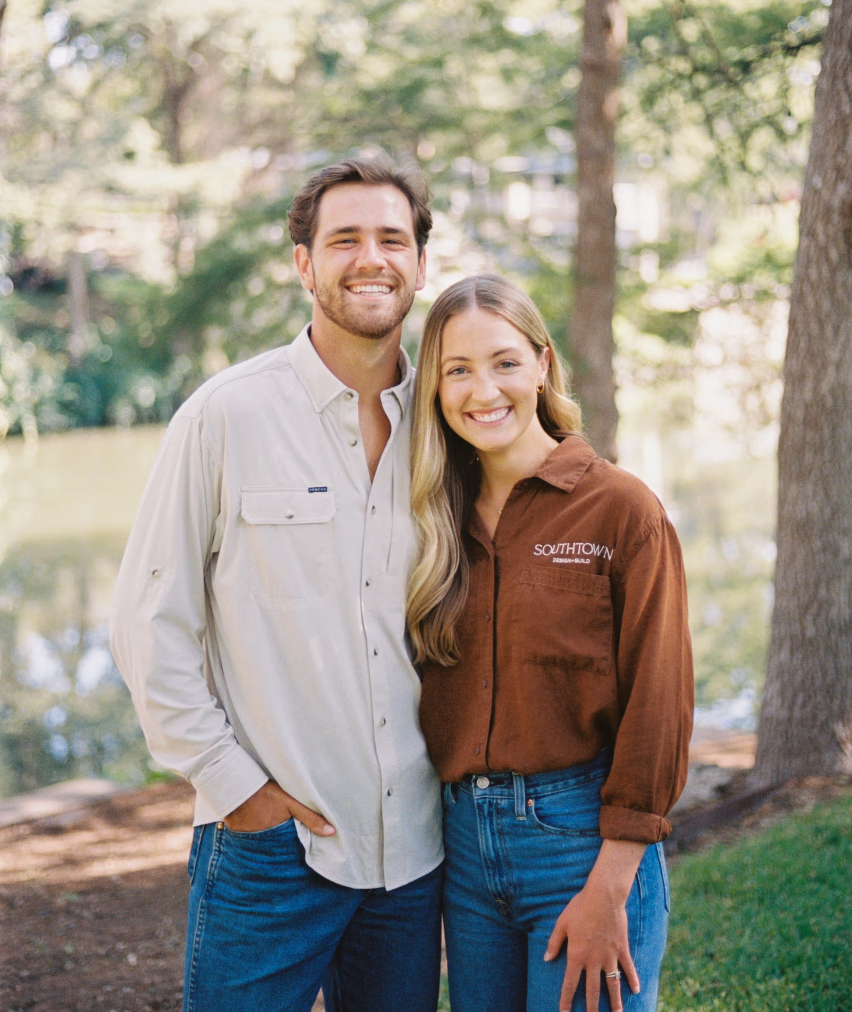Smiling man and woman standing outdoors near trees and water, the woman wearing a brown shirt with Southtown Design-Build logo.