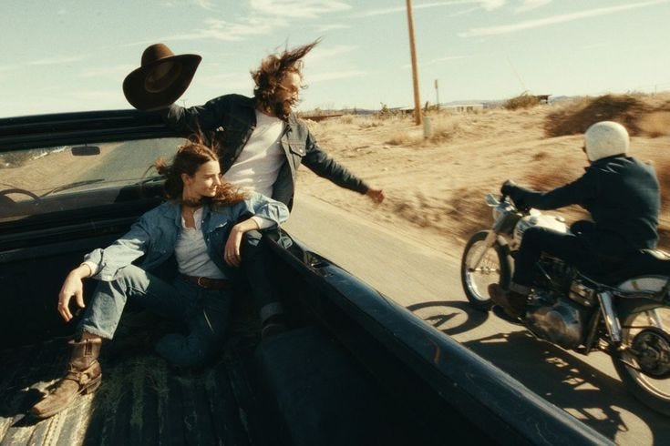 This may contain: two people riding in the back of a pick up truck with a motorcycle behind them