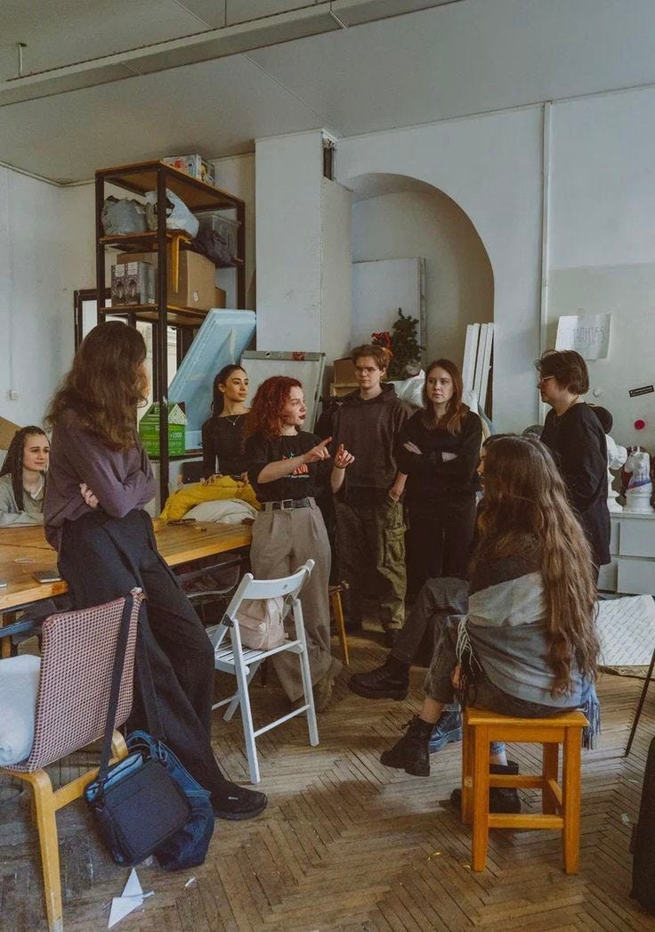 This may contain: a group of people standing around a wooden table in a room with many other people