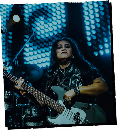 Musician playing an electric bass guitar on stage with blue circular lights in the background.
