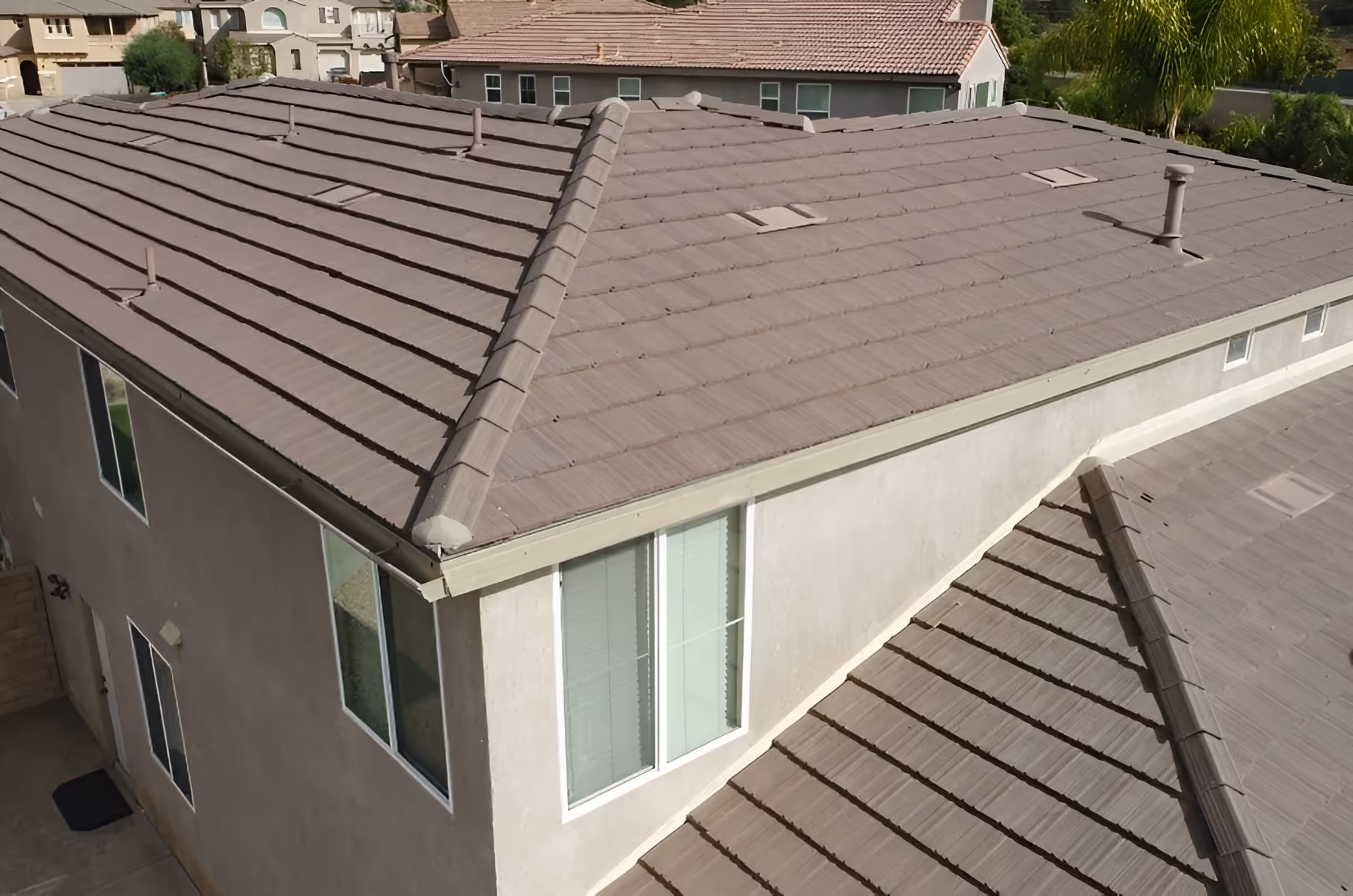 Aerial view of a house with a brown tiled roof, beige walls, and visible roof vents.