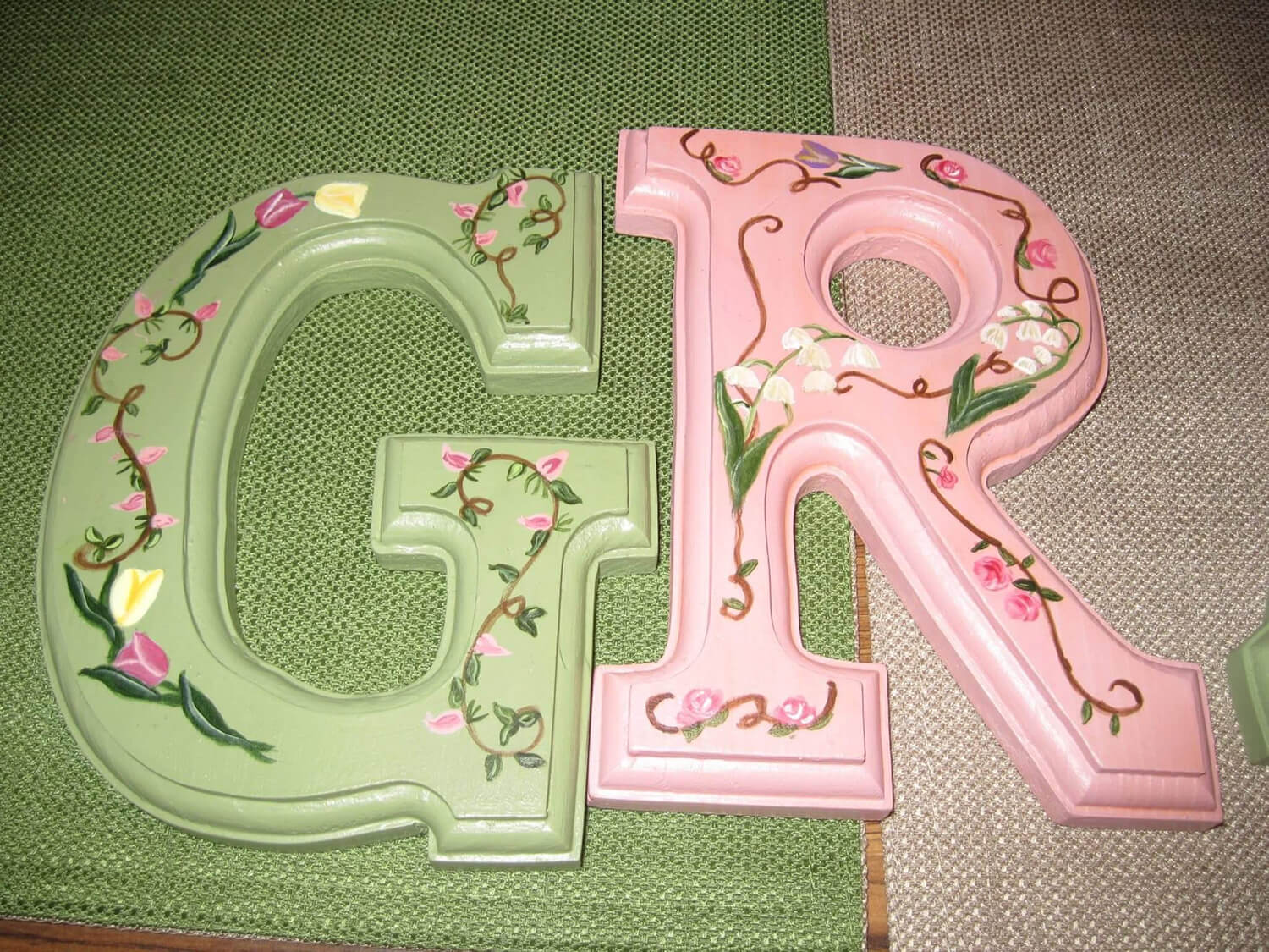 Decorative painted wooden letters "G" and "R" in green and pink with floral vine designs.