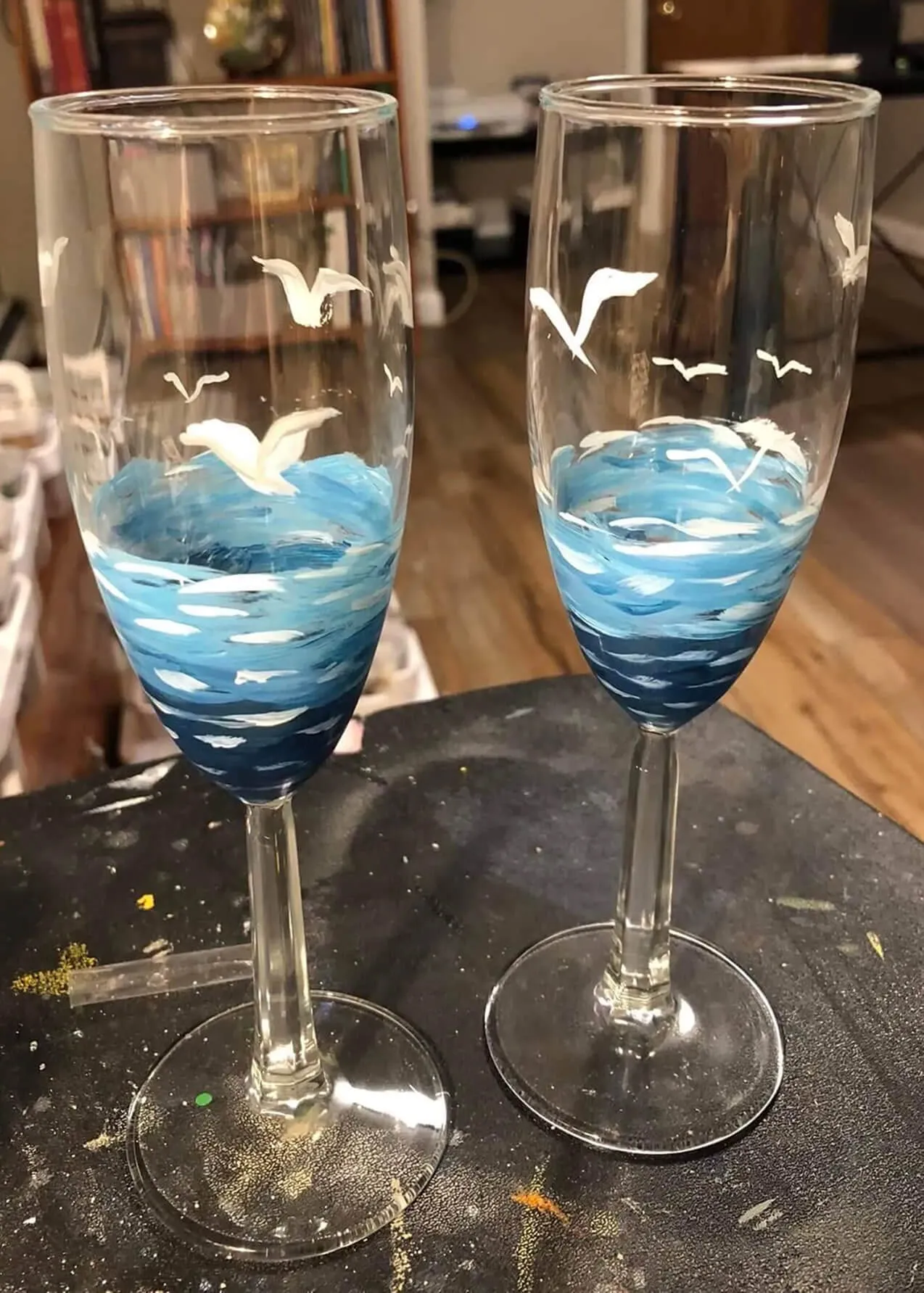 Two champagne flutes hand-painted with stylized blue ocean waves and white seagulls.