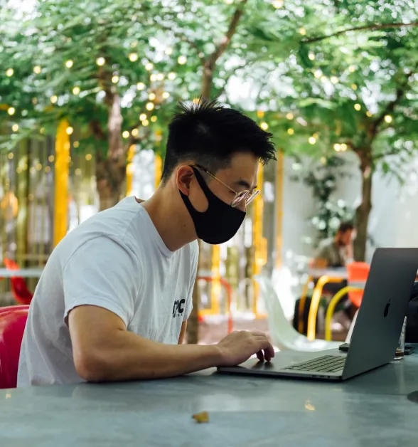 Asian man outdoors at a table working on laptop.