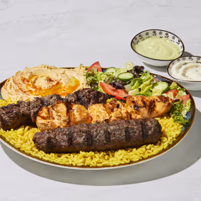 Mixed grill combo on a plate with salad, hummus, rice and white and green sauce.