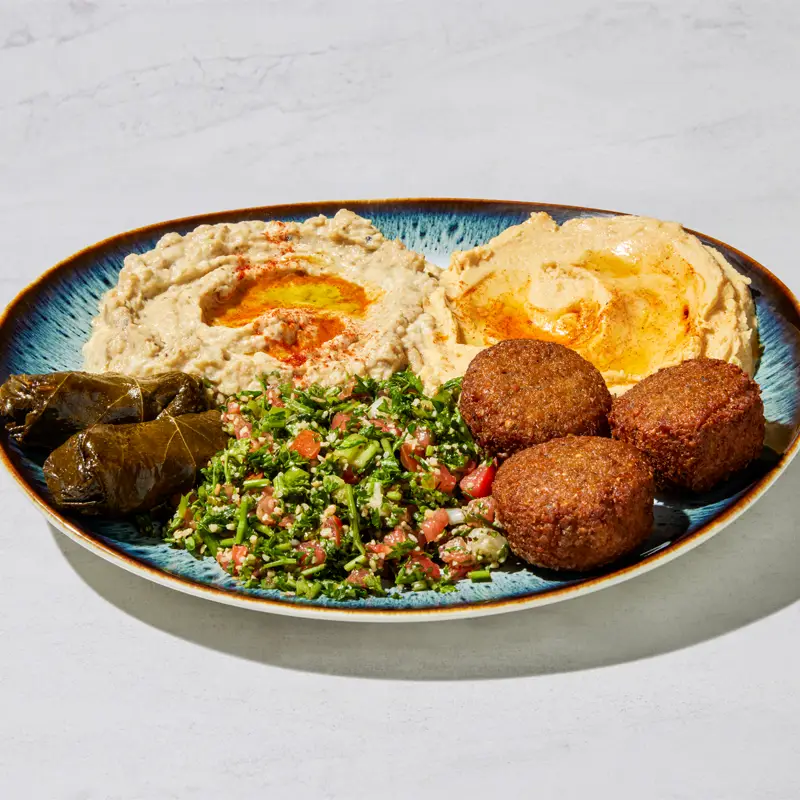 A colorful vegetarian platter with falafel, hummus, baba ghanoush, grape leaves, and salad from The Green Olive.