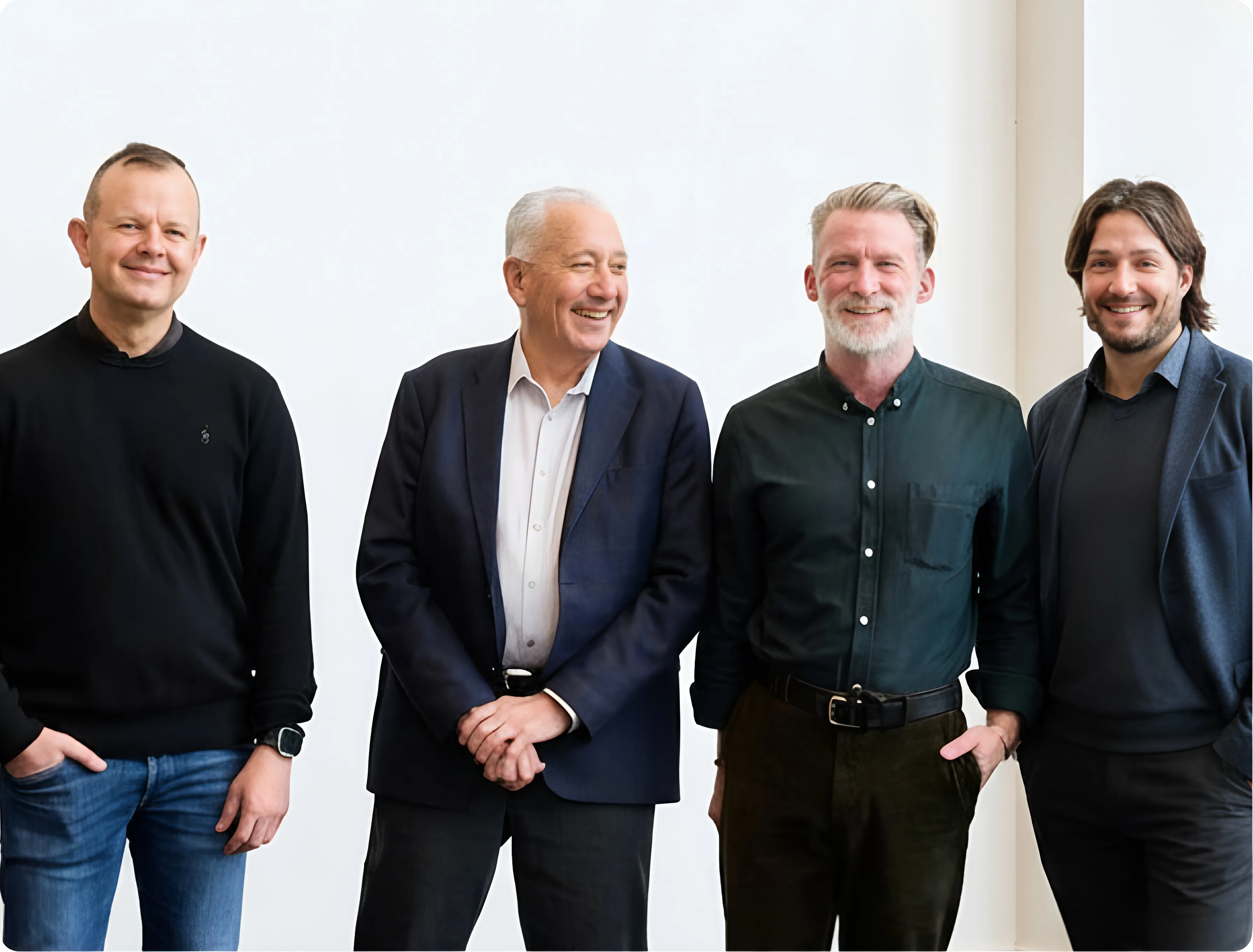 Four men standing and smiling in business casual attire against a white background.