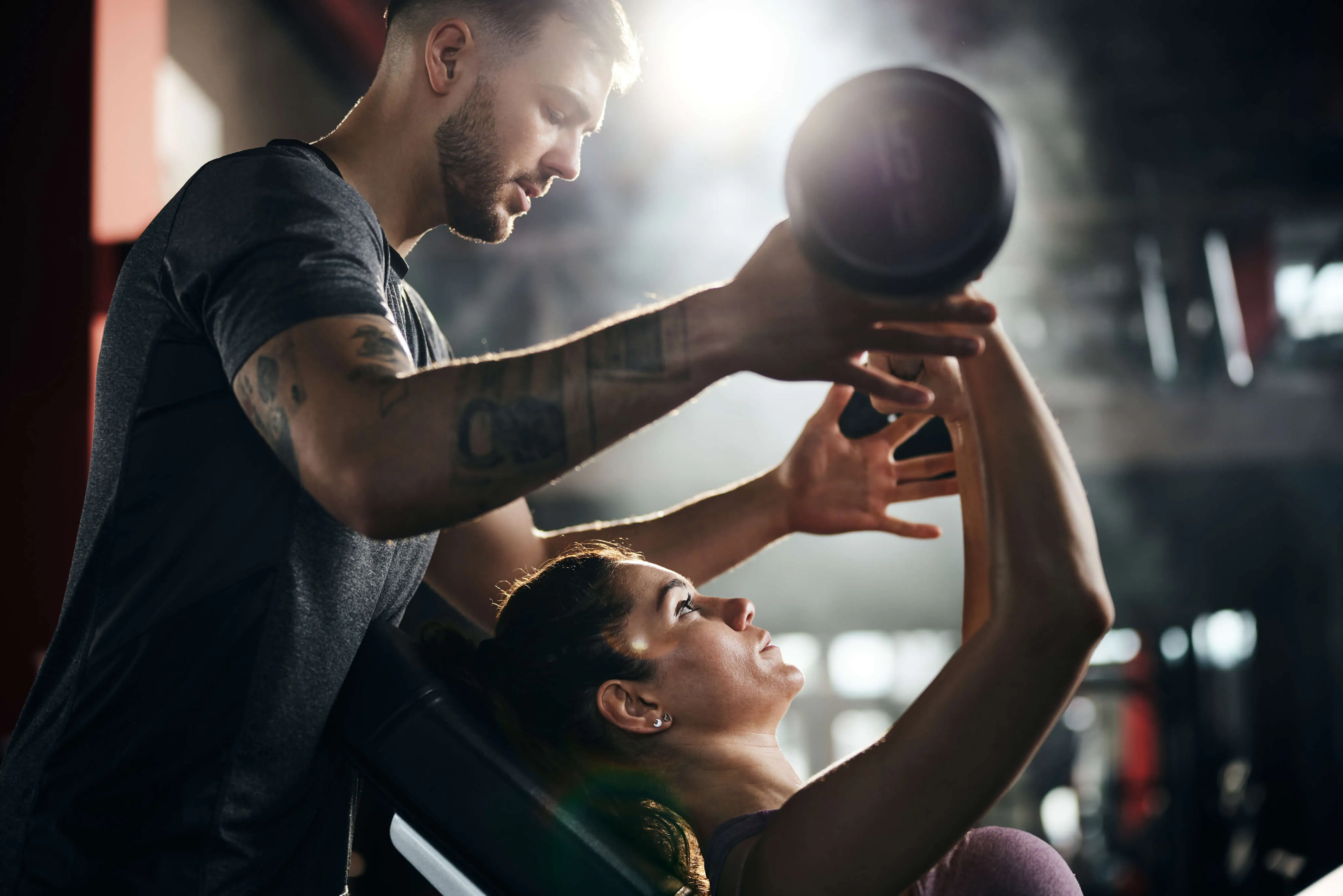Personal trainer and client lifting weights in a gym on a bench