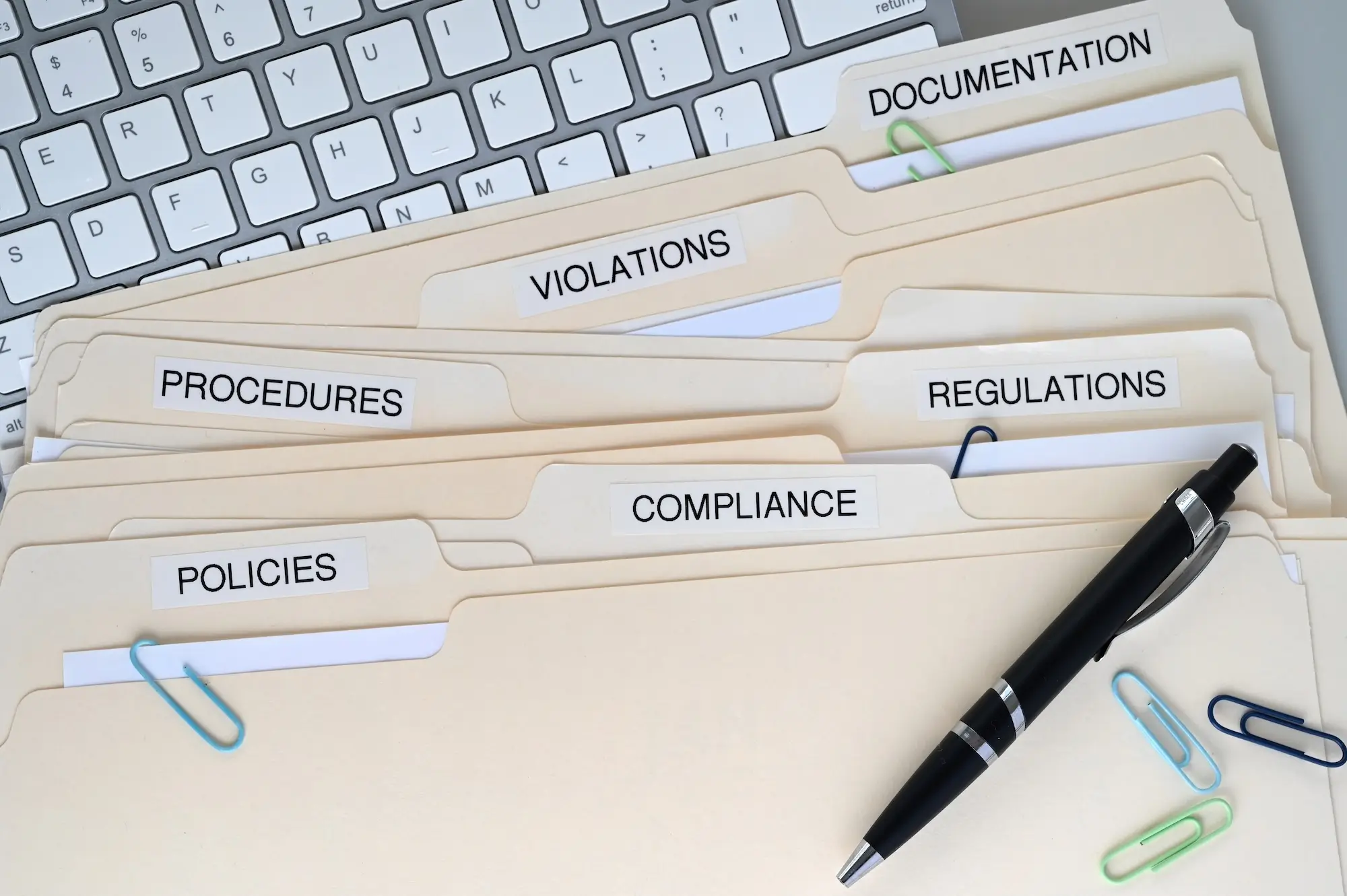 A stack of folders containing  policies, procedures, and regulations to ensure compliance
