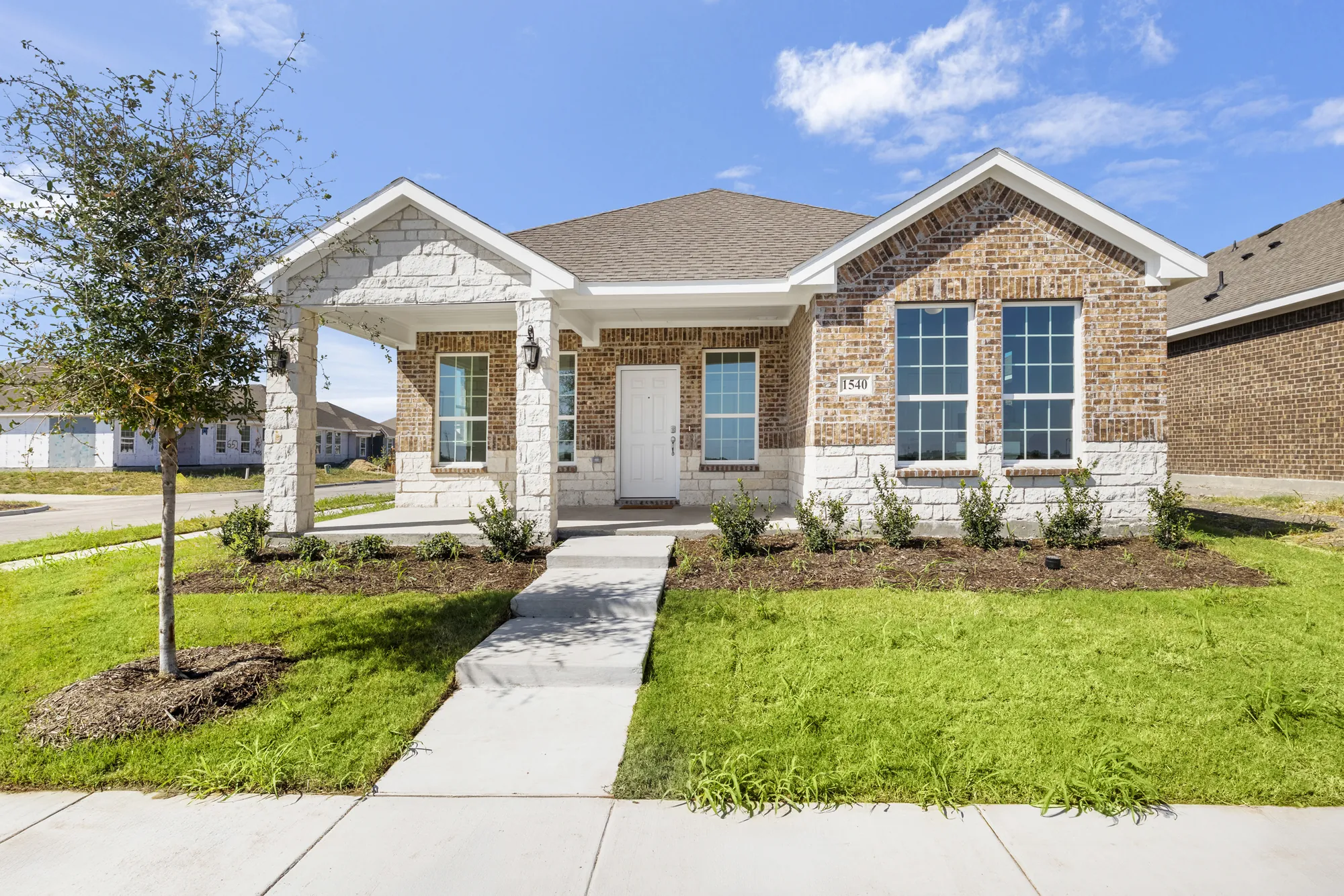 Front of a new single-story brick and stone Camden home with a covered porch in Camden Park, Waxahachie, Texas