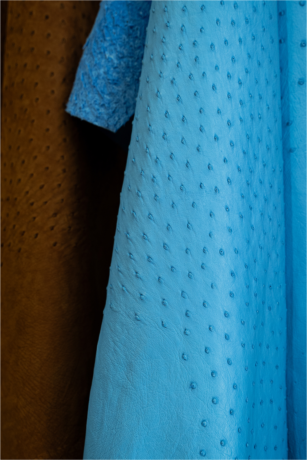 Close-up view of two pieces of fabric hanging side by side. One is a textured baby blue material with small raised dots, and the other is a smooth brown fabric. The focus is on the details and textures of the fabrics.