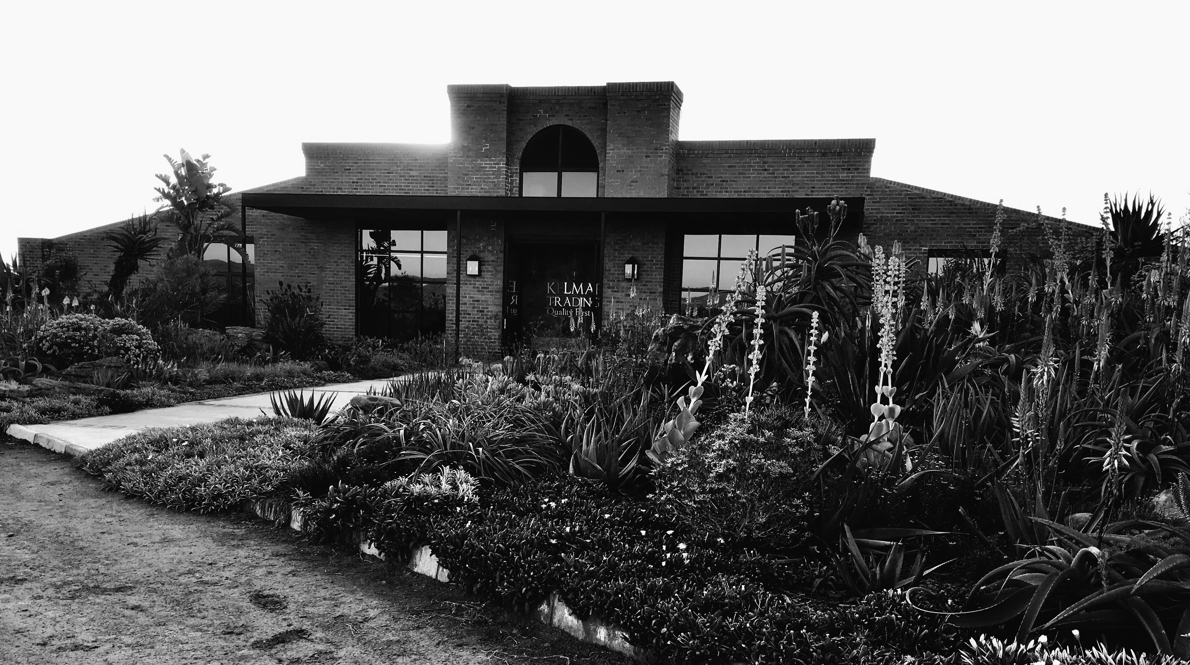 Front view of a brick building with large windows and a garden filled with tall flowering plants and succulents.