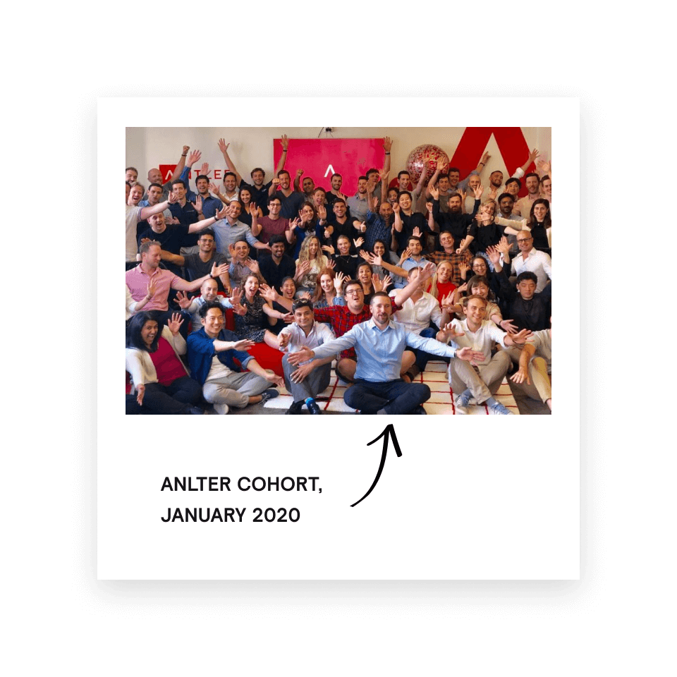 Group photo of a diverse cohort of people smiling and raising their hands together indoors.