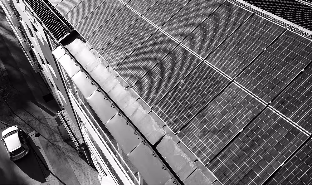 A rooftop covered with rows of solar panels viewed from an elevated angle, with a street and a white car visible below.
