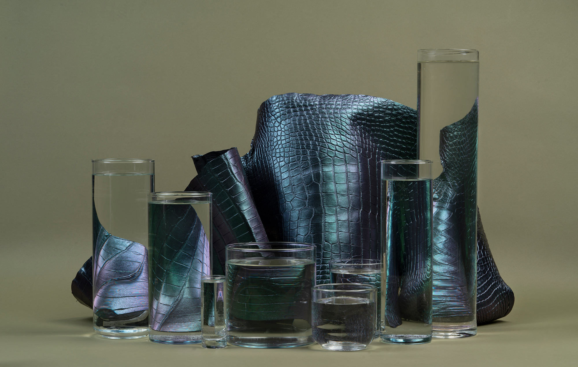 Two pieces of textured green leather, one rolled and the other partially unrolled, placed next to a large green monstera leaf against a dark background.
