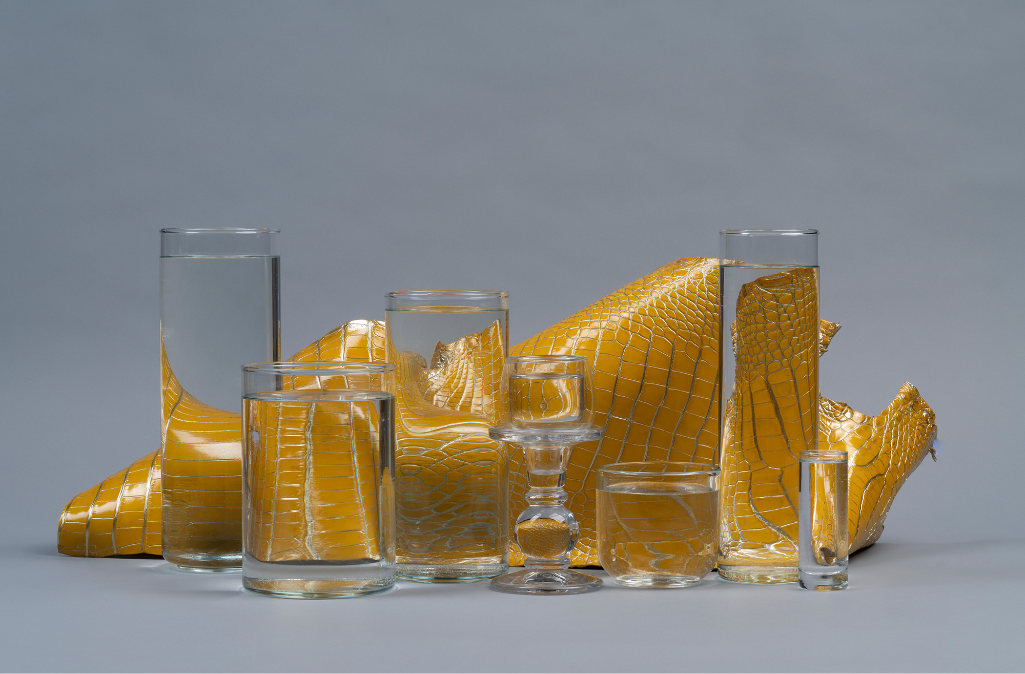 Two pieces of textured green leather, one rolled and the other partially unrolled, placed next to a large green monstera leaf against a dark background.