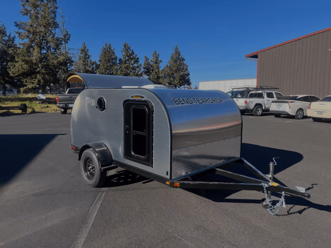 A modern, silver camping trailer parked at a campsite.