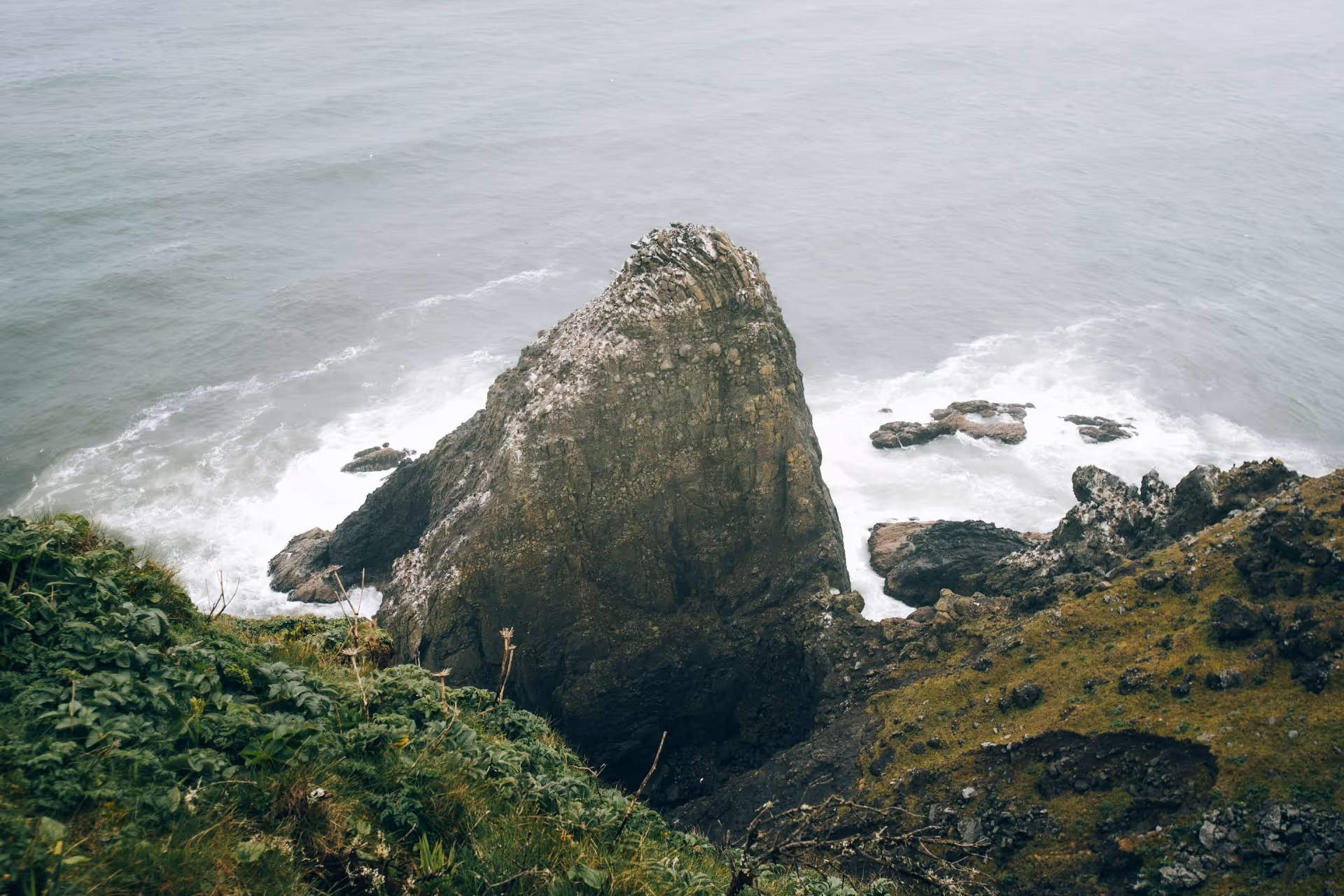 An aerial view of a rugged coastline with large rock formations rising out of the sea.