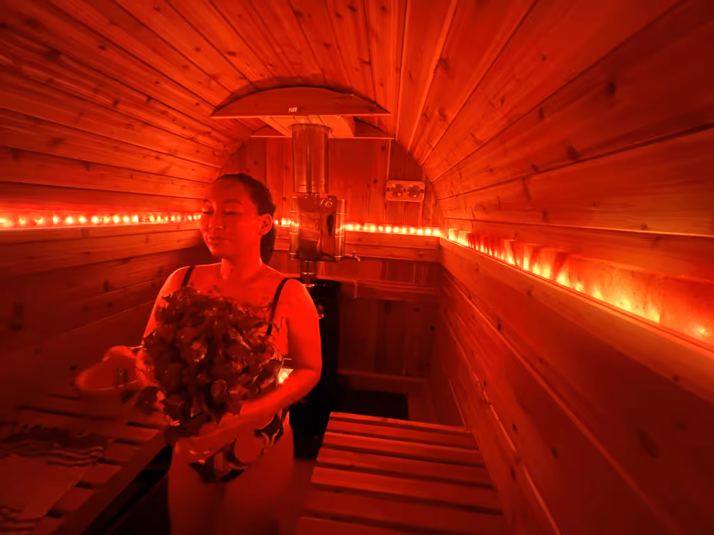 The silhouette of a person sitting inside a barrel sauna that is illuminated with a saturated red light.