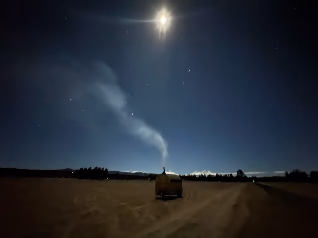 A clear night sky filled with stars and a bright moon over a dark, silhouetted landscape.