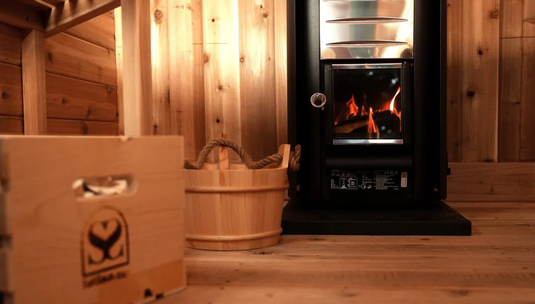 The interior of a sauna featuring a small, black wood-burning stove with a protective grate.