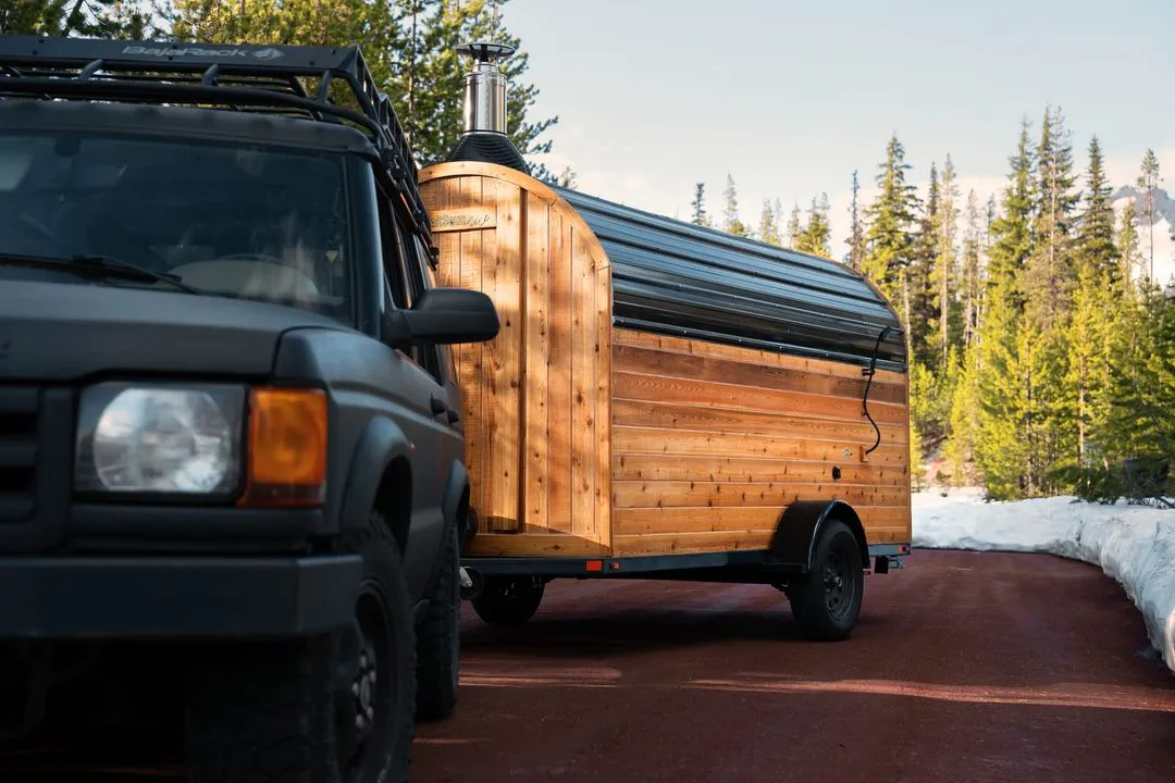 A semi-truck hauling a mobile sauna on a trailer along a highway.