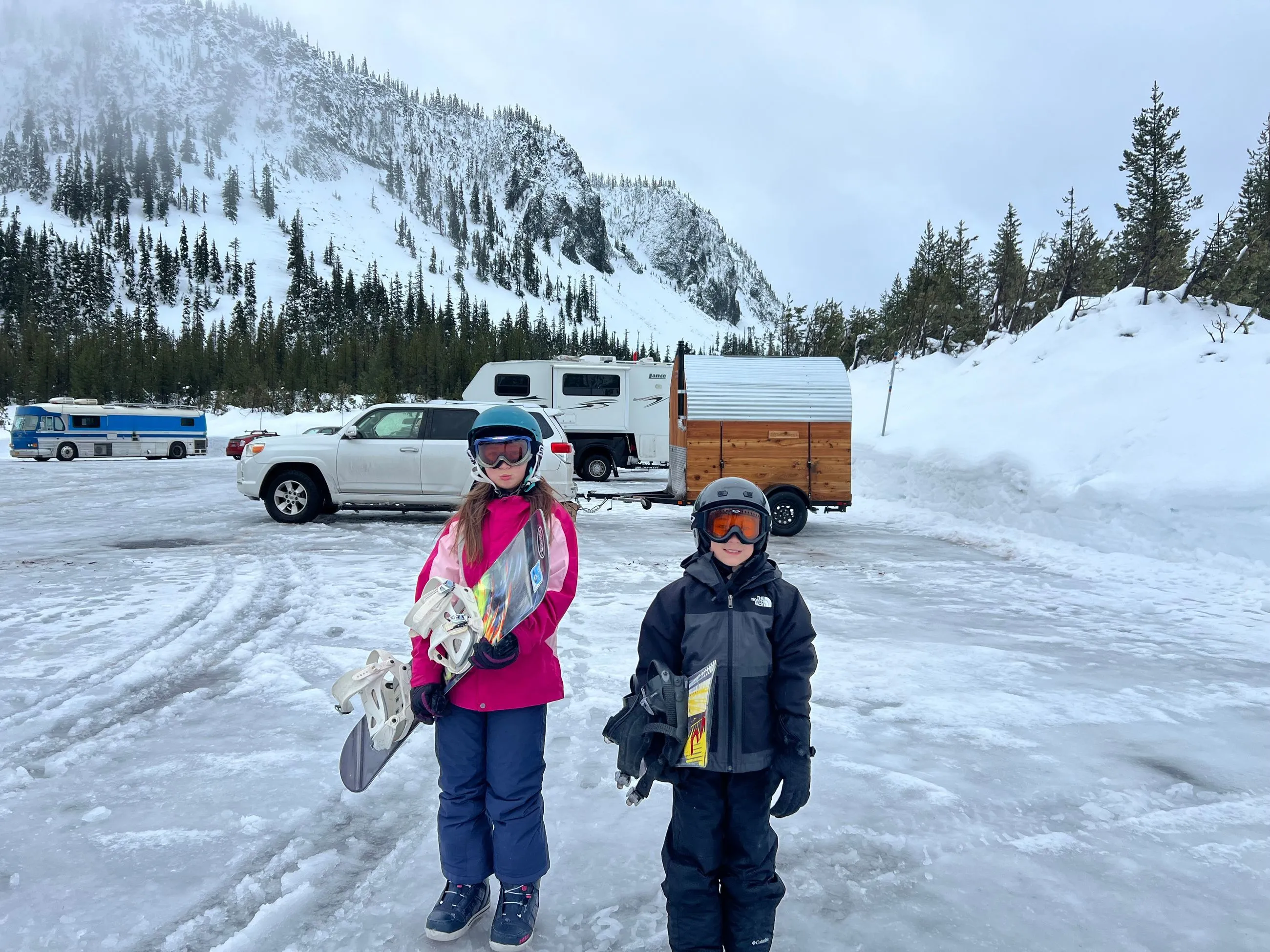 Two people stand in a vast, snowy landscape with mountains rising in the background.