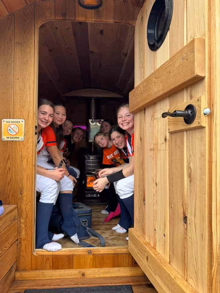 A happy group of people are crowded into the doorway of a sauna, smiling for a picture.