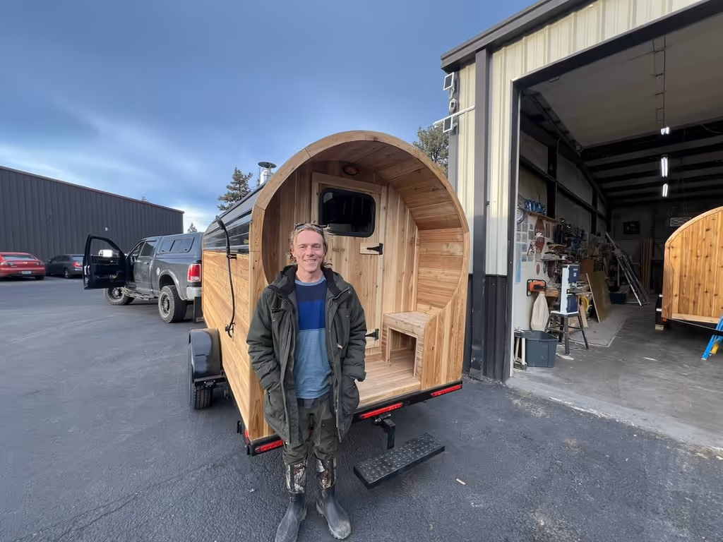 A man standing in front of a wooden horse trailer.