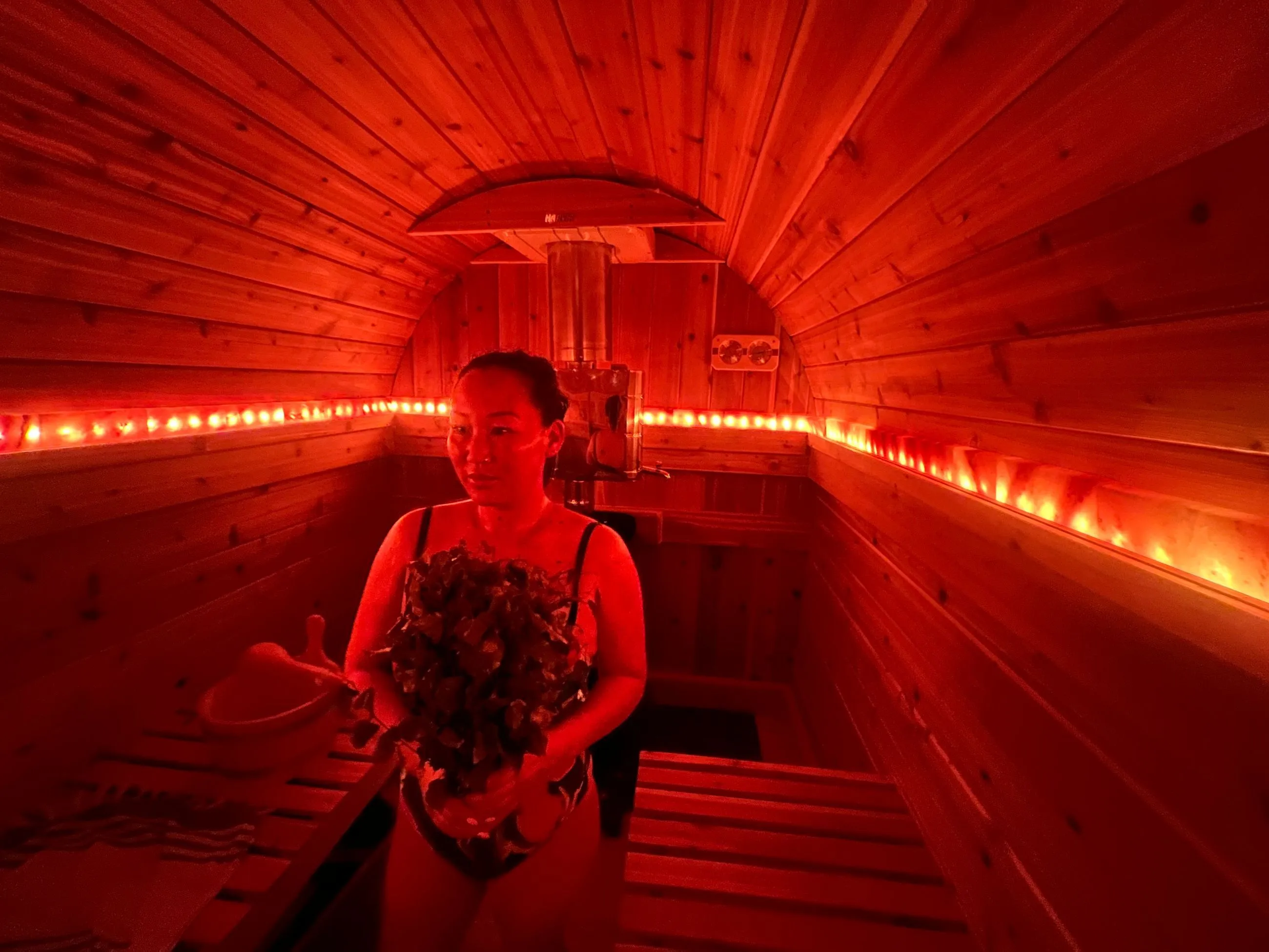 The interior of a barrel sauna glows with intense red-orange light, showing a person sitting inside.