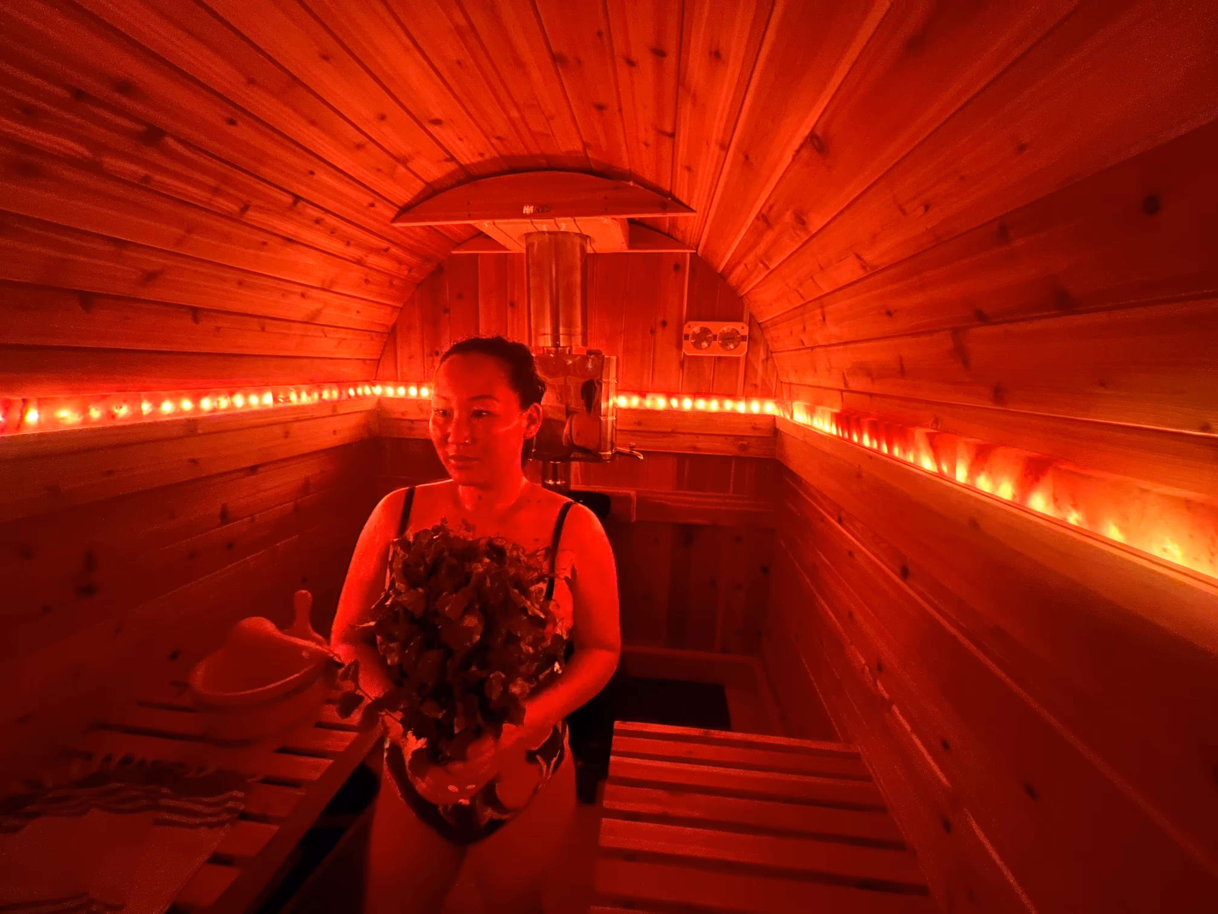 The interior of a barrel sauna glows with intense red-orange light, showing a person sitting inside.