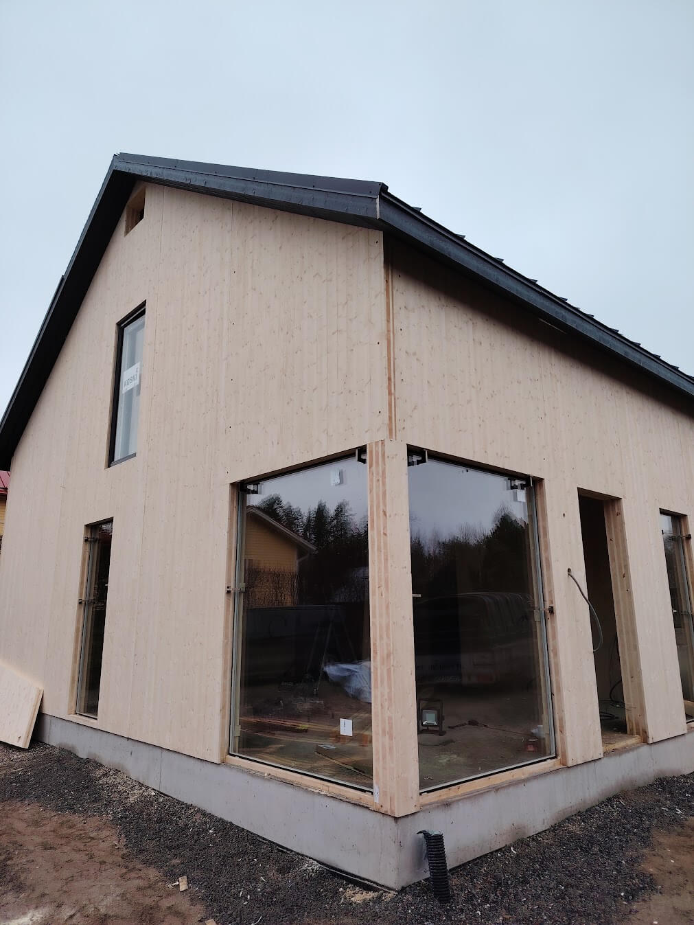 Keskenään rakennettu vaalea puurakenteinen talo harmaalla katolla ja suurilla ikkunoilla.
