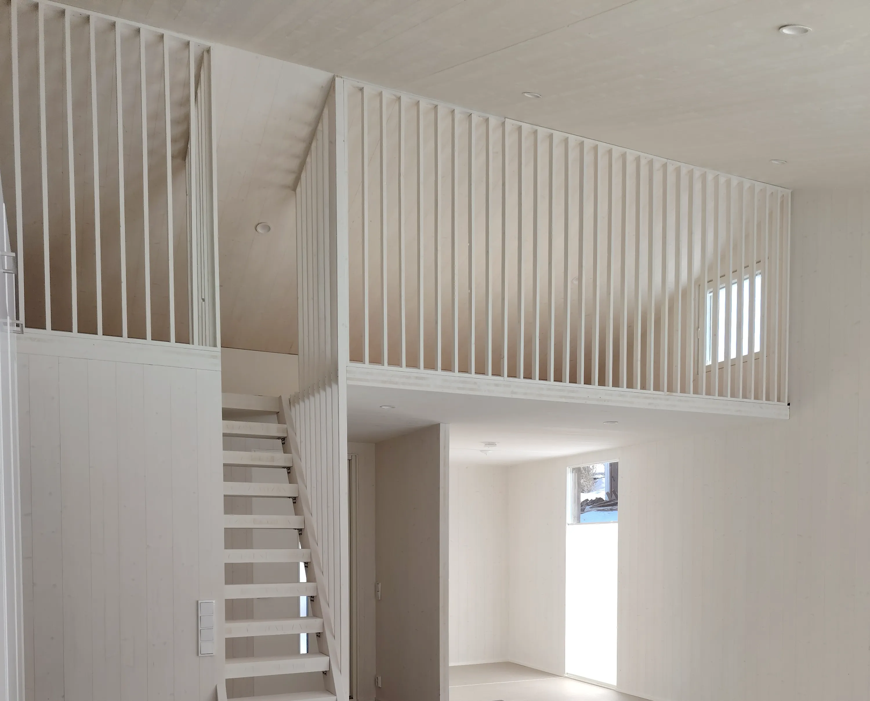 Vaalean puun värinen sisätila, jossa on parvi, portaat ja valkoiset seinät.