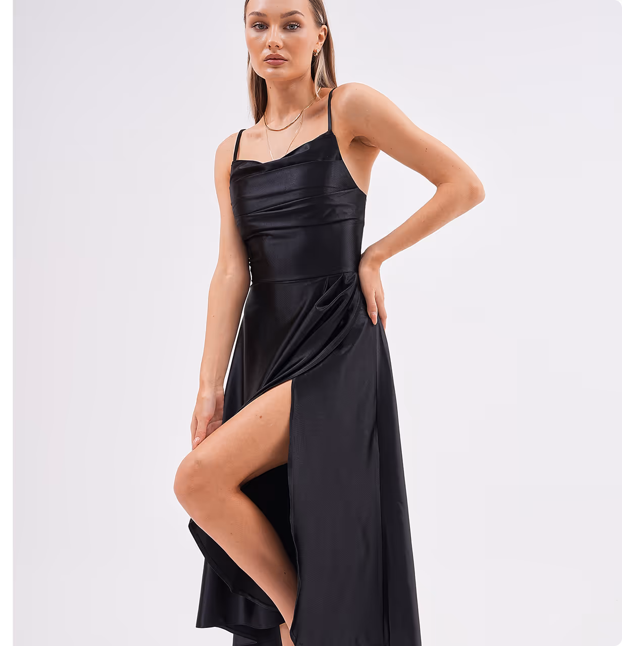 Model in Celestera black satin gown showing side slit detail, posing with hand on hip.