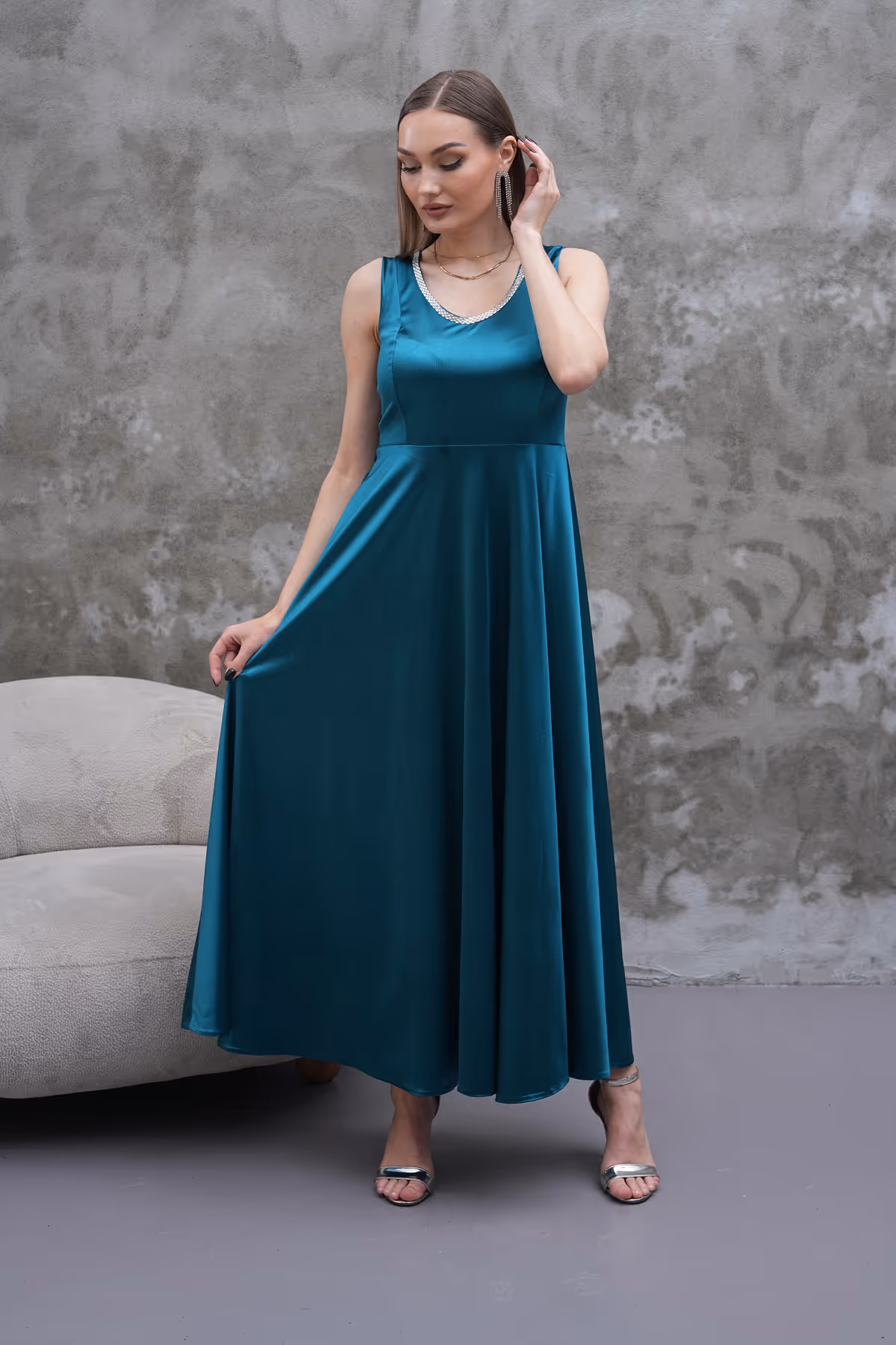 Model posing in Liona teal dress with hands holding the skirt, highlighting its sleeveless bodice and elegant drape.