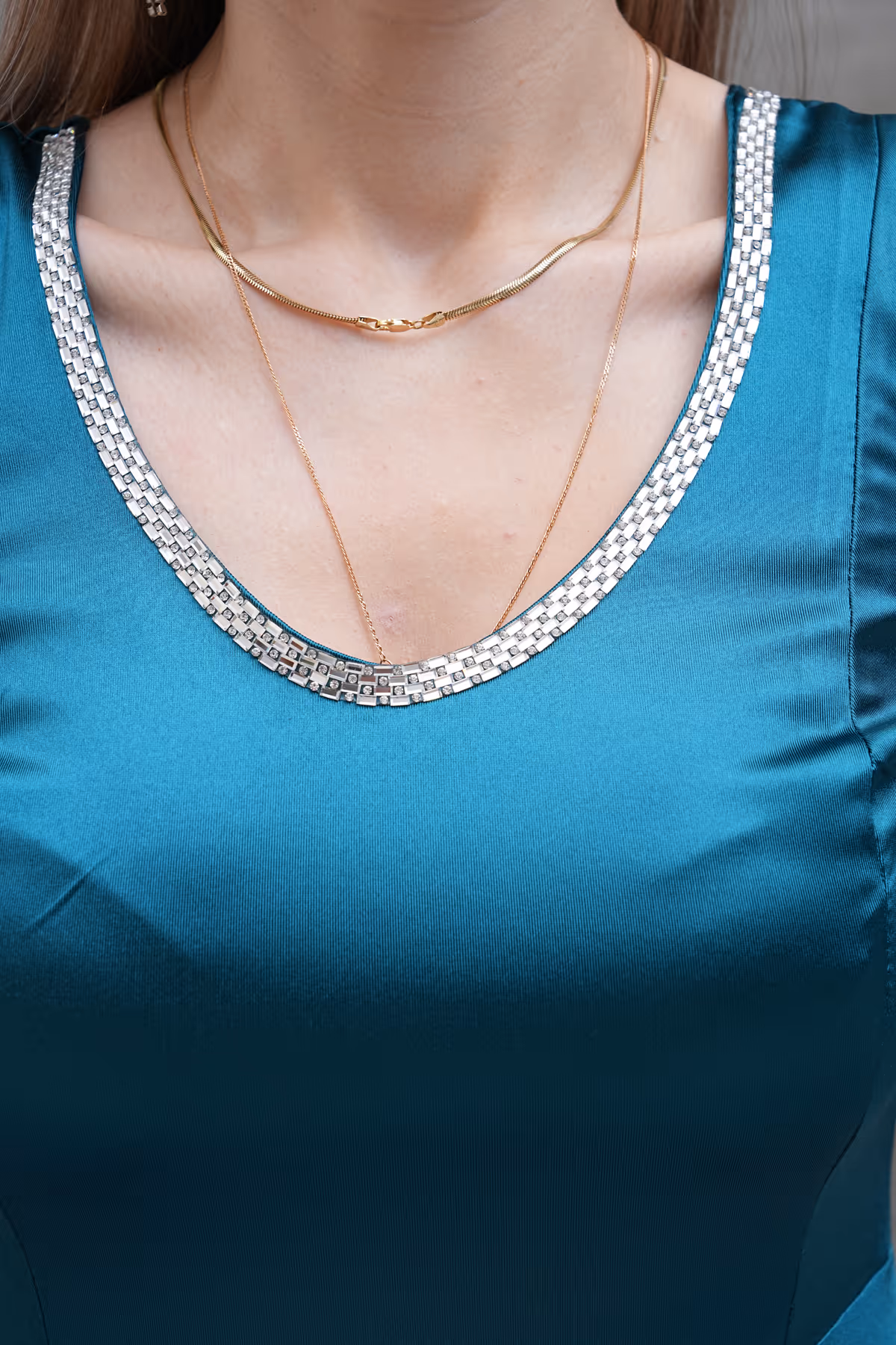 Close-up of Liona gown’s embellished scoop neckline in teal satin, accented with layered gold necklaces.