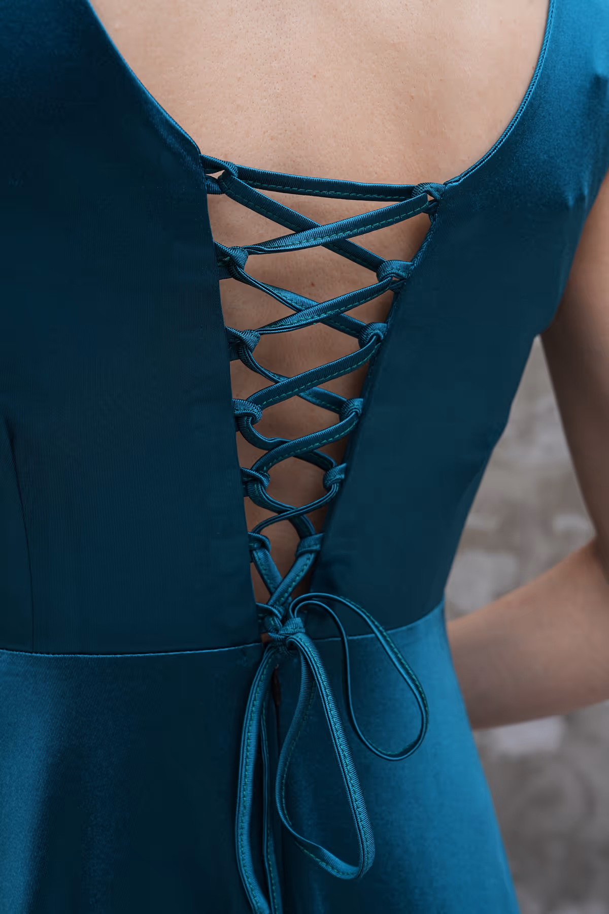 Back view showing the adjustable lace-up detail of the Liona satin gown in teal, tied into a neat bow.