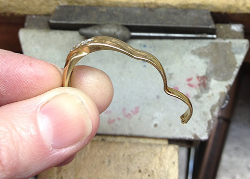 Close-up of a jeweler holding a bent gold ring, preparing it for repair or reshaping on a bench block