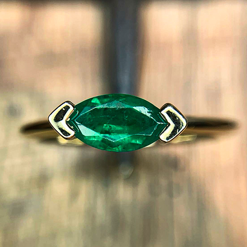 Minimalist gold ring featuring a marquise-cut emerald held by open chevron prongs