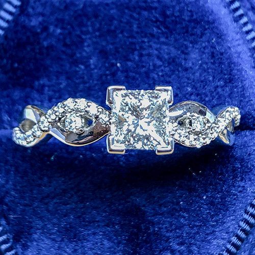 Intricate diamond engagement ring with a square-cut center stone and twisted band design, displayed in a royal blue velvet box