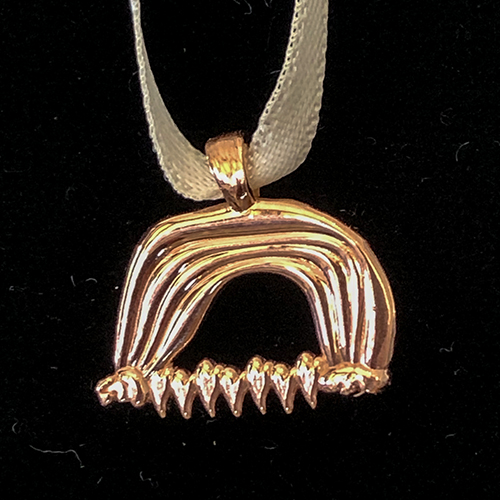 Abstract gold pendant resembling an arched form with textured ridges and pointed elements, displayed on a fabric cord