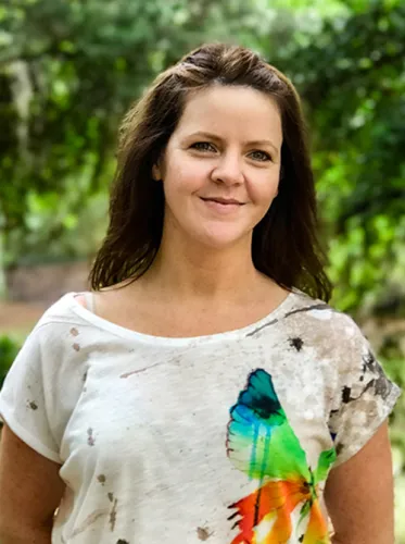 Elizabeth Schindler, owner and goldsmith at Esch Metals Studio, smiling outdoors in a colorful butterfly shirt