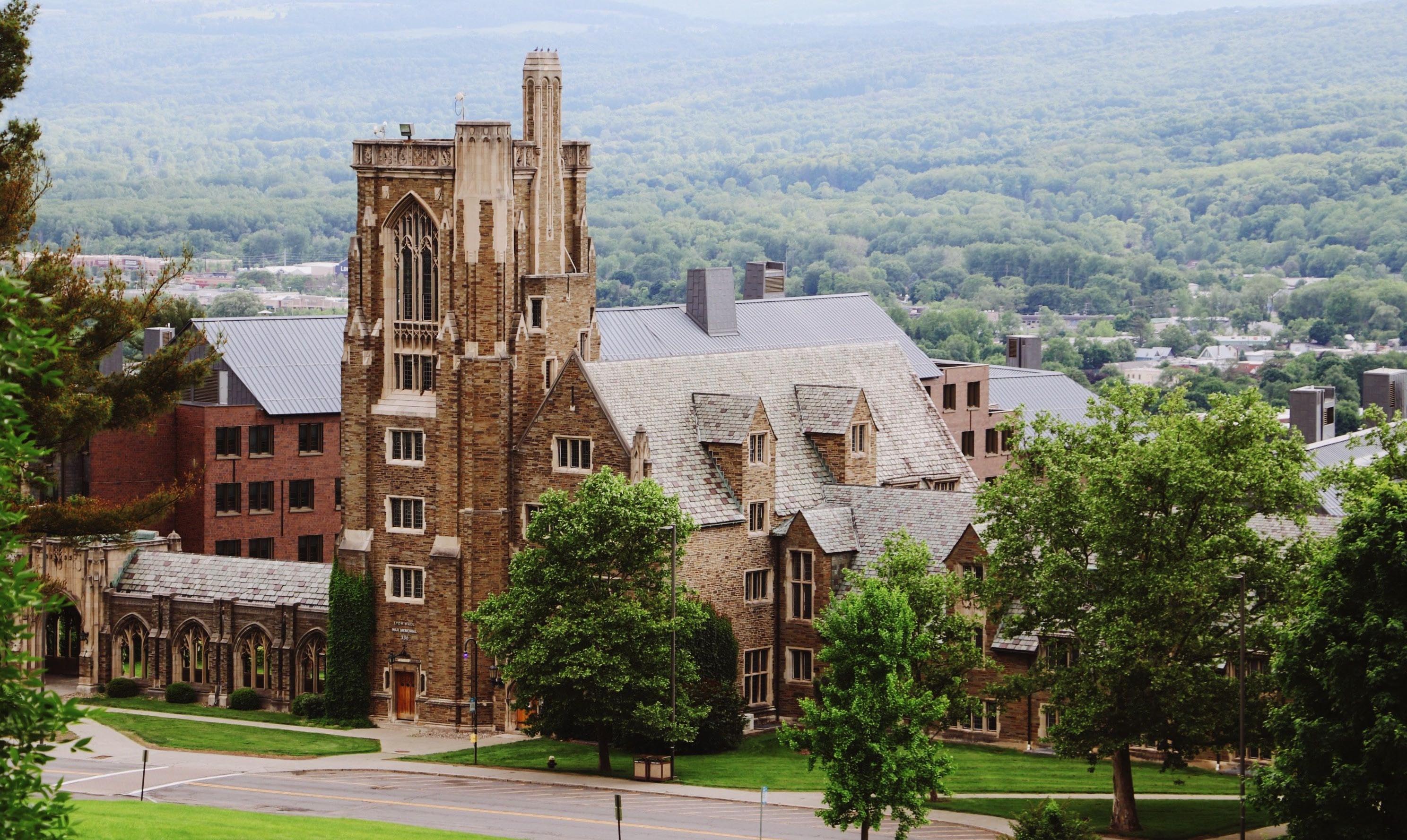 Cornell University, a red brick building set against rolling green hills of grass.