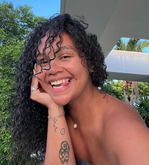A young dark-curly haired woman smiling at the camera