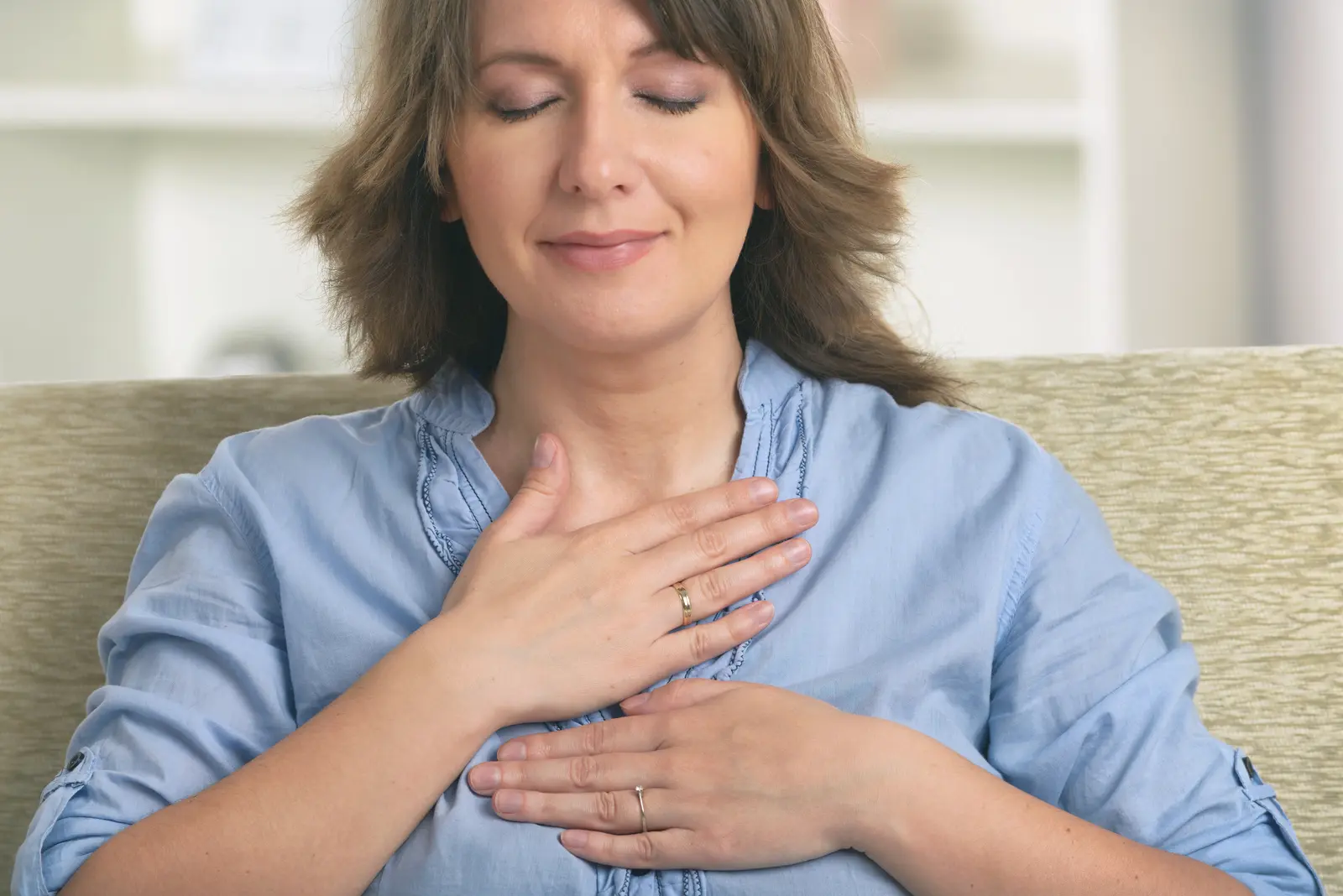 Femme souriante assise dans son canapé, les mains posées sur le coeur